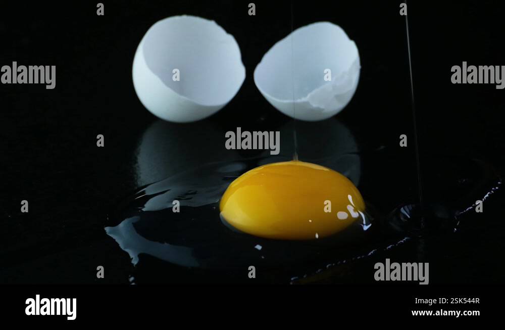 Duck egg cracked onto a black reflective surface, yoke dripping down ...