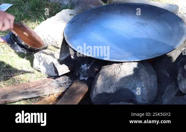 Chef uses bellows to stoke fire under a large pan on a makeshift ...