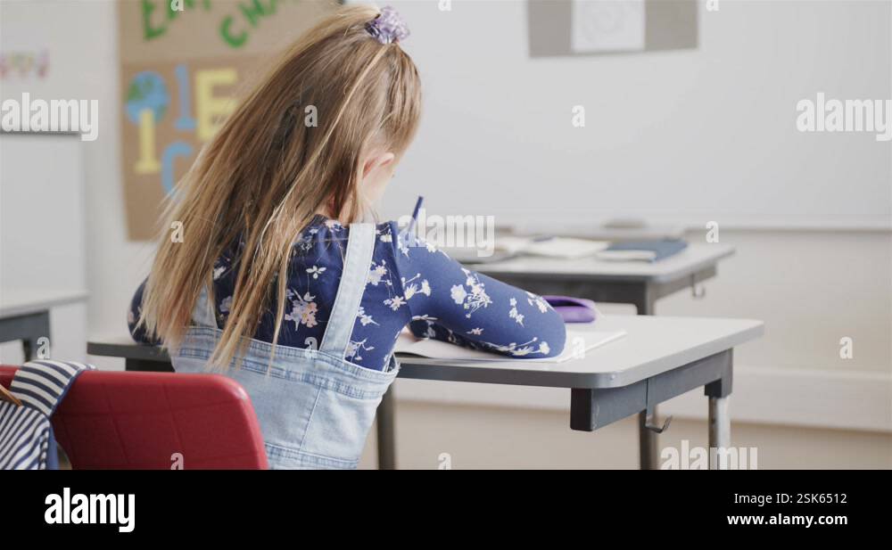 Rear view of caucasian schoolgirl writing at desk in elementary school ...