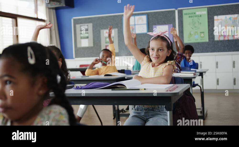 Happy diverse schoolchildren at desks raising hands in elementary ...