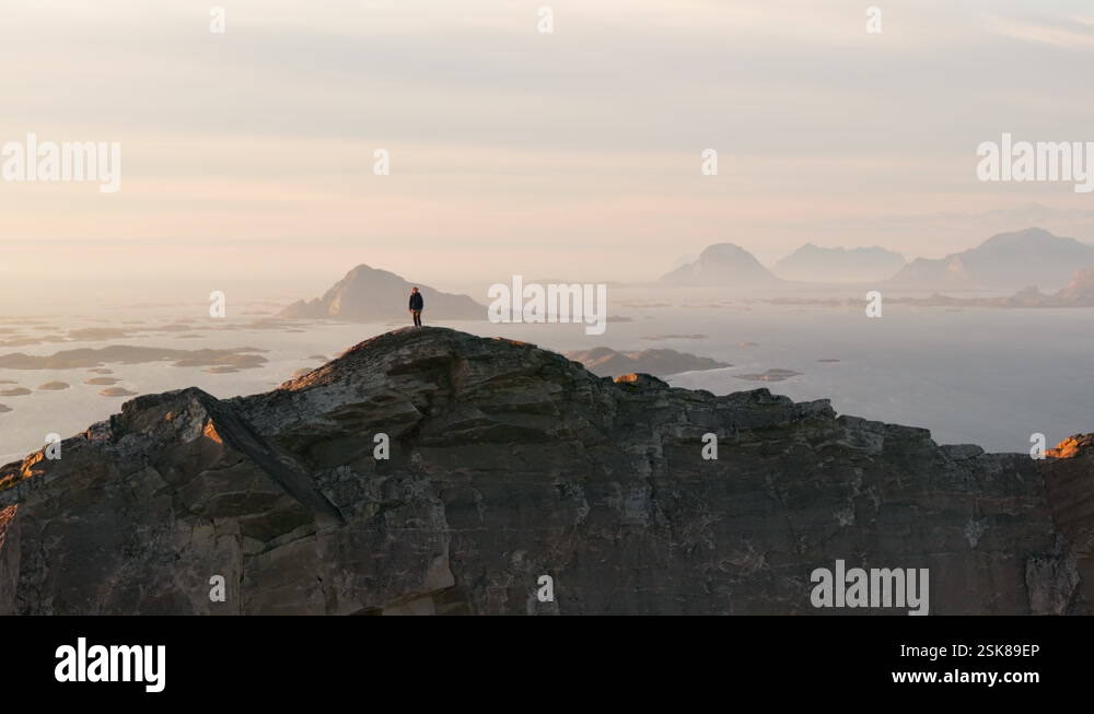 Man on coastal arctic mountain ridge in Norway midnight sun glow; drone ...