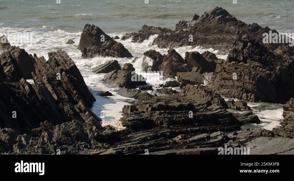 mid shot of sea breaking and crashing over jagged sedimentary rocks in ...