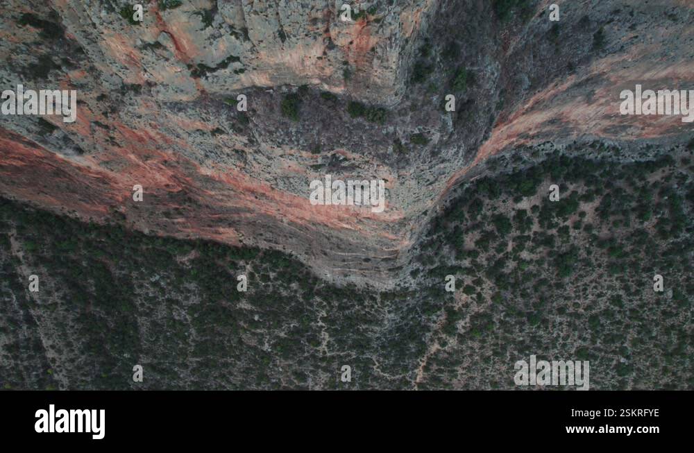 Drone top down descends across intimidating sheer cliff face with dry ...