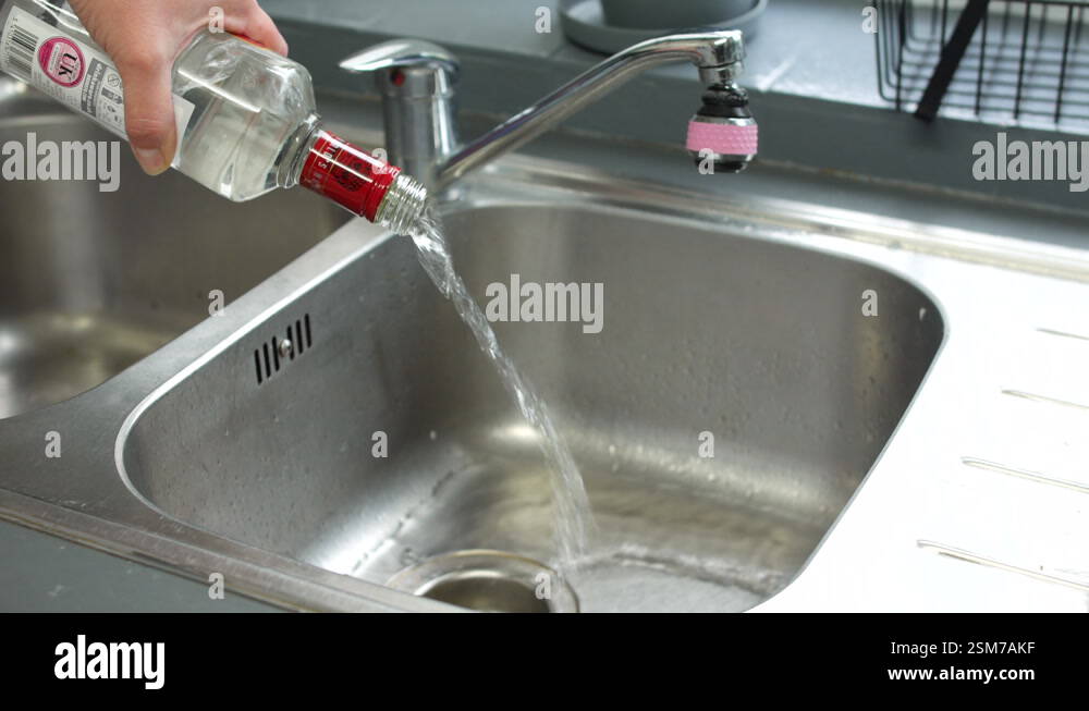 Alcoholic pouring away vodka down the drain of a sink giving up and ...