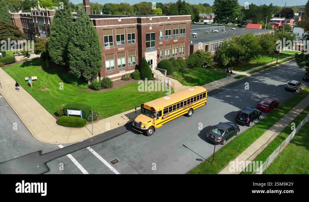 School bus driving next to brick American school. Aerial tracking shot ...