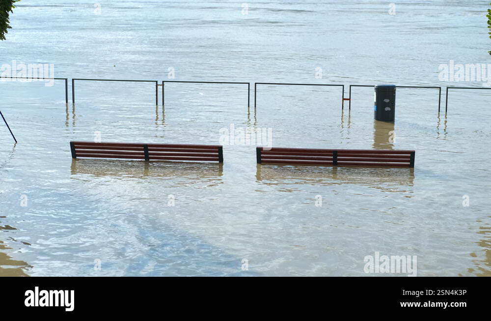 Flood. Rising river water submerging benches and trash can along the ...