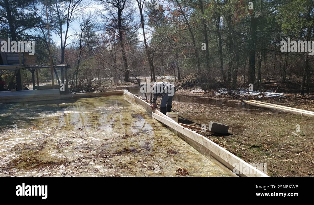 Skinny man dismantling melted home made ice rink in the backyard Stock ...