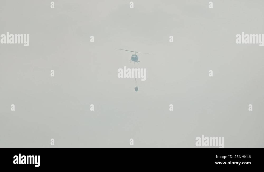 Chopper Small Fly A chopper flies in thick smoke carrying a water bucket for firefighting ...