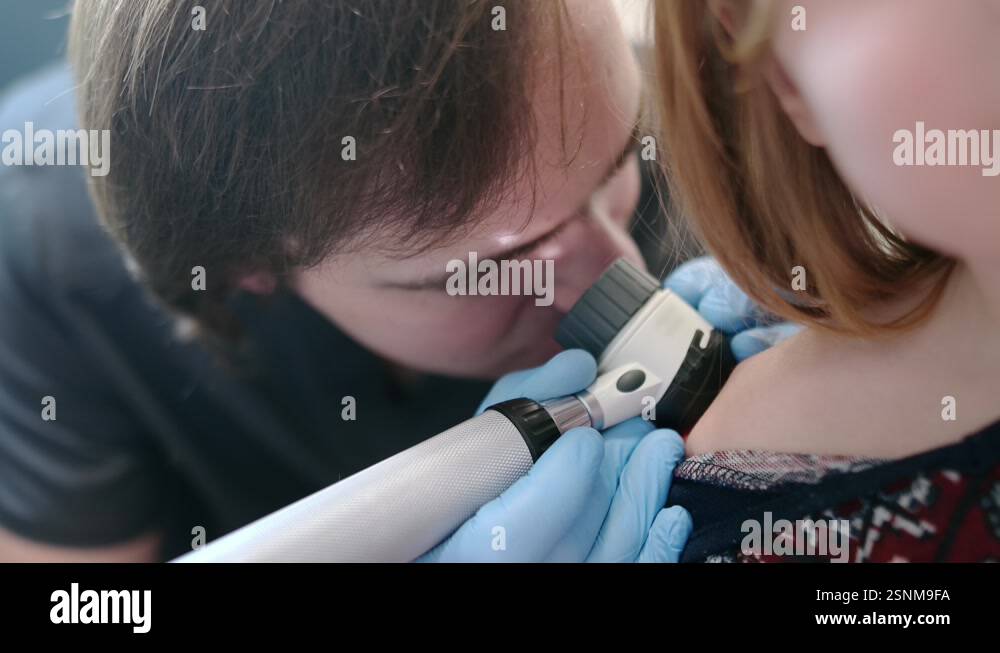 A dermatologist looks at a rash on the back of a girl using a ...
