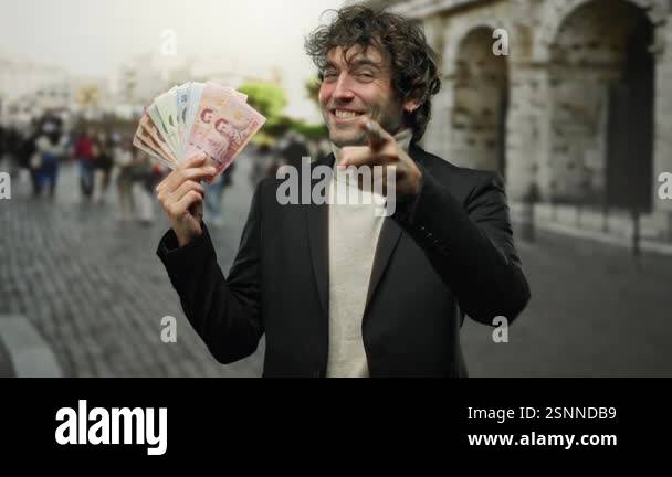 Man outdoors in a city holding thai banknotes, making a call gesture ...