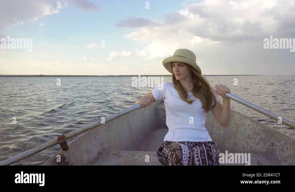 Beautiful young woman rower in straw hat sailing slowly on paddle boat ...