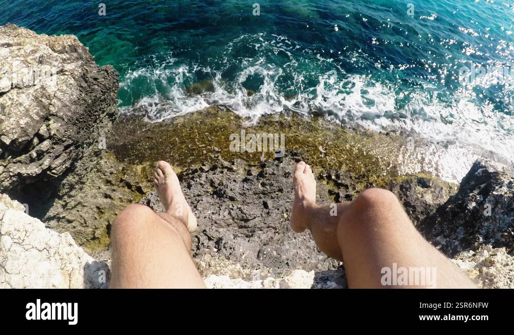 First person perspective of young male explorer sitting on rock cliff ...