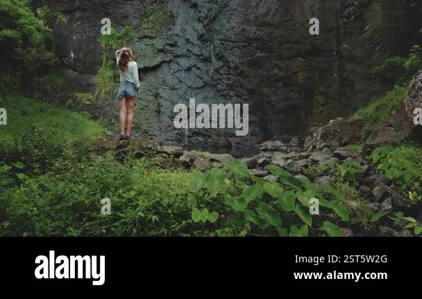 Tourist woman stands on a rock enjoy cascading waterfall in tropical ...