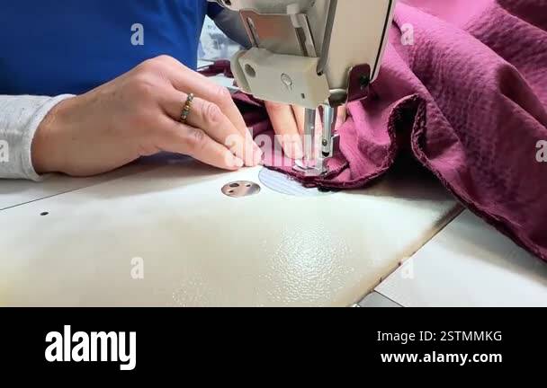 Close-up of hands guiding fabric through an industrial sewing machine ...