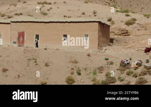 A woman walks past a simple earthen house in a rural desert area of ...