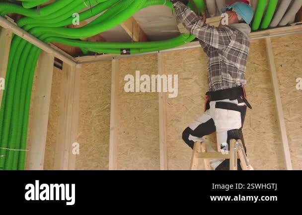 A skilled worker adjusts bright green ducting within the frame of a new ...
