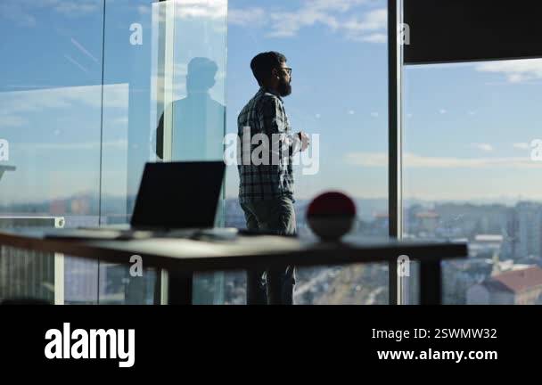Thoughtful Indian businessman stands at window, drinks coffee and ...