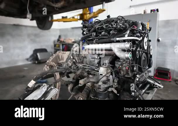 A car engine sits on a stand in a mechanic shop. The car is lifted on a ...