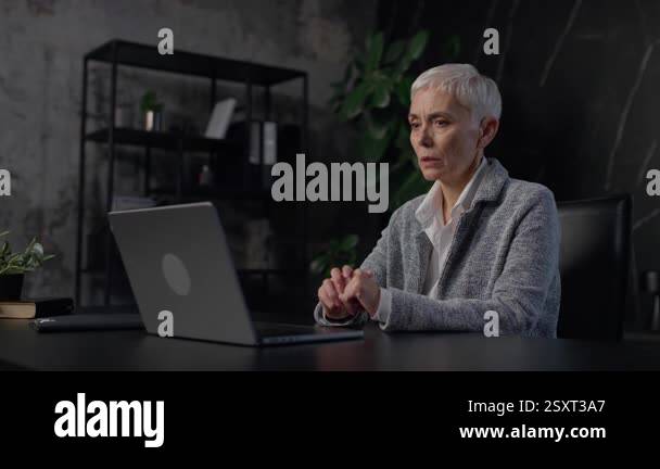 a-senior-professional-woman-sitting-at-a-dark-office-desk-engaged-in-a-virtual-meeting-on-her-laptop-appearing-concerned-and-focused-on-the-discussion-2sxt3a7.jpg