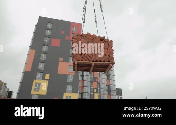 Crane lifting a pallet of bricks at a construction site, A pallet of ...