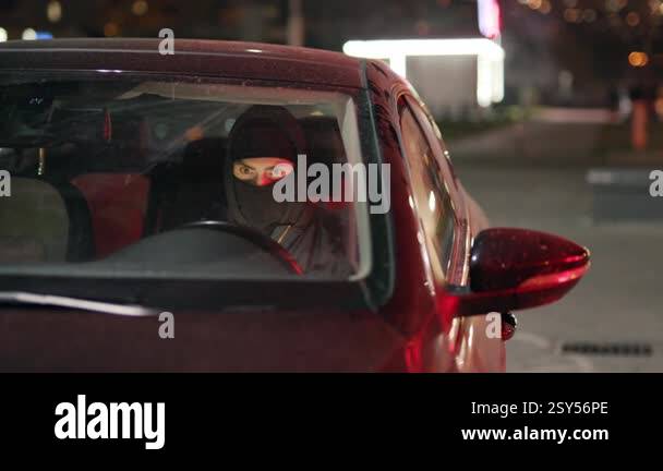 A mysterious, masked individual sits quietly in a parked vehicle ...