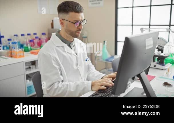 A young man with a beard working on a computer in a laboratory setting ...