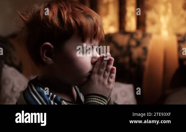 A young boy is praying in a dark room. A red-haired boy of seven to ten ...