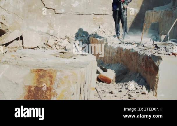 Working male builder at a stone quarry crushes stone with a rock-drill ...