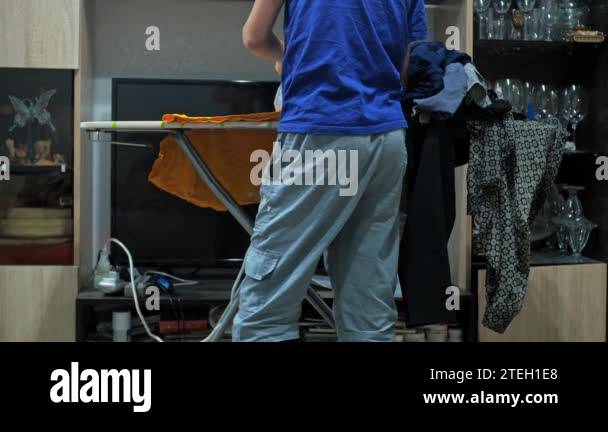 a boy ironing a T-shirt with an iron. housework. theres a pile of
