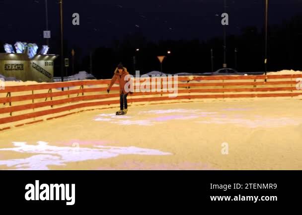 A man is skating on an ice skating rink in winter under a snowfall ...