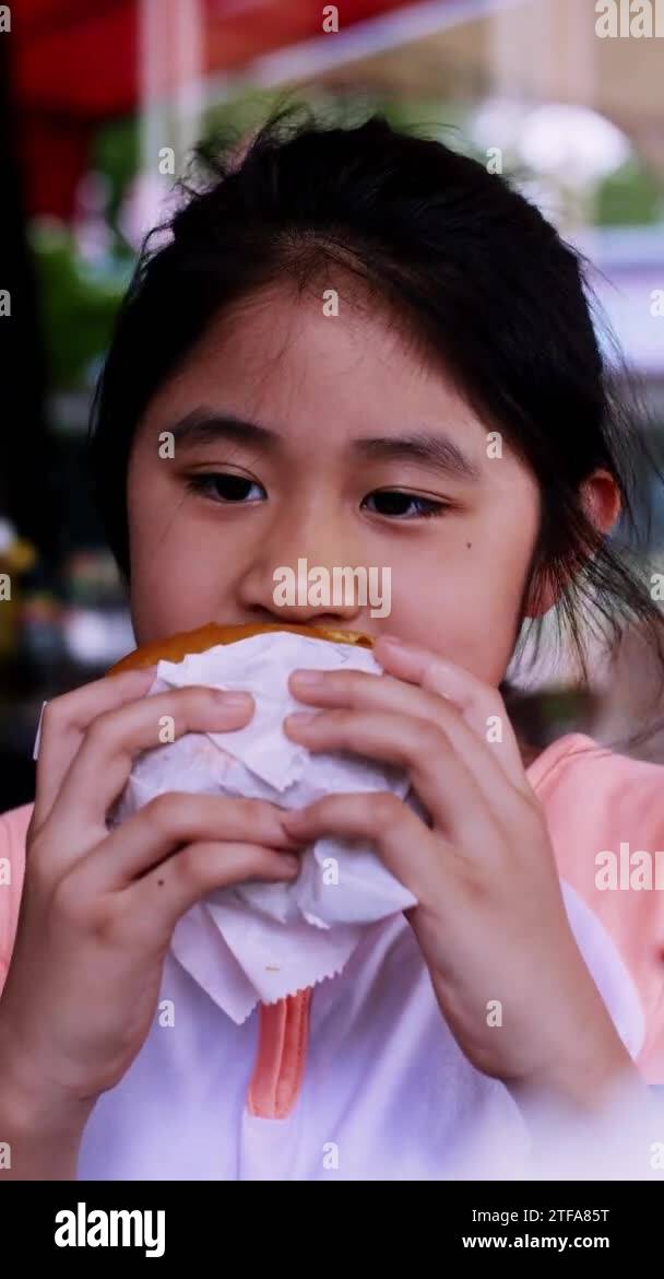 Vertical footage. Little girl in fast food cafe eats burger. Hungry ...