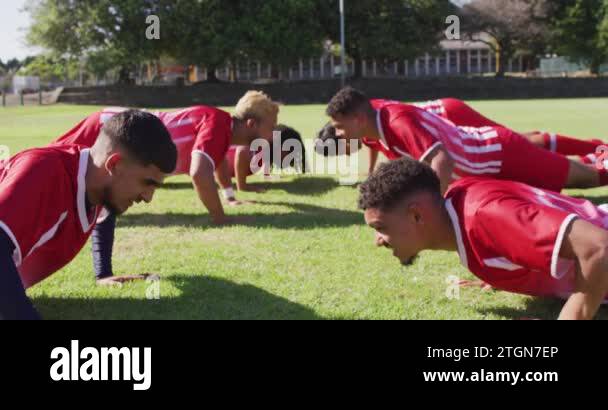Diverse group of male football players warming up on field, doing push