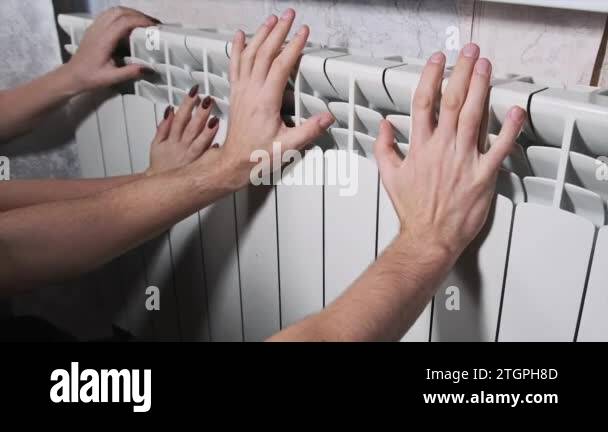 Frozen male and female hands touch the home radiator and try to warm up ...