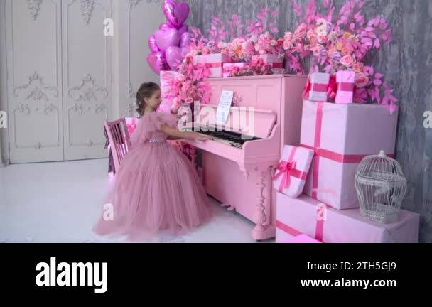 Beautiful little girl in pink dress sitting on a chair and playing the ...