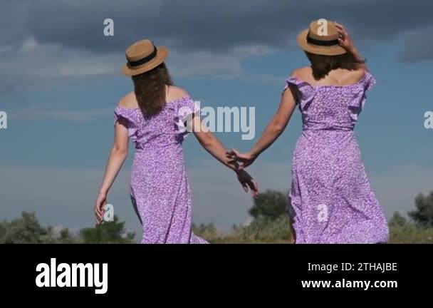 Back view of young twins sisters in summer dresses and straw hats ...
