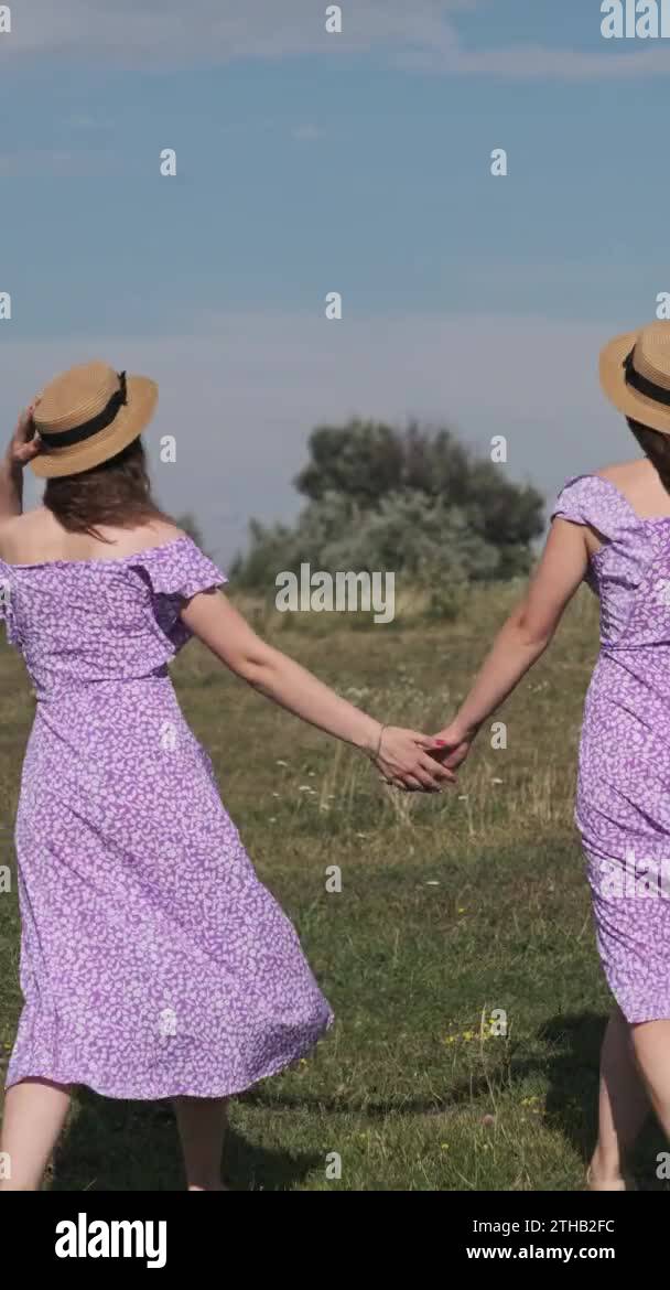 Vertical, Back view of young twins sisters in summer dresses and straw ...