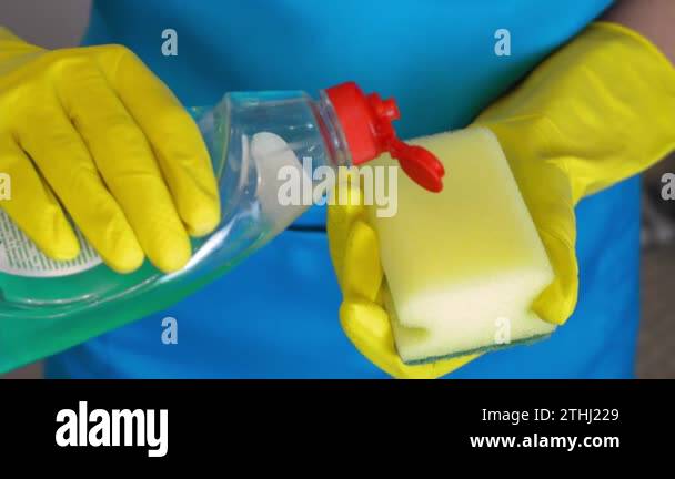 Hands in yellow gloves apply drop of dish detergent from plastic b-sash ...
