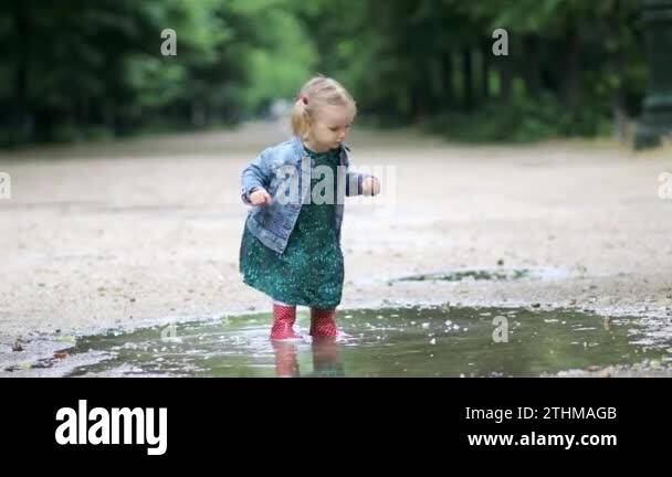 Child wearing red rain boots and jumping in puddle on a summer day ...