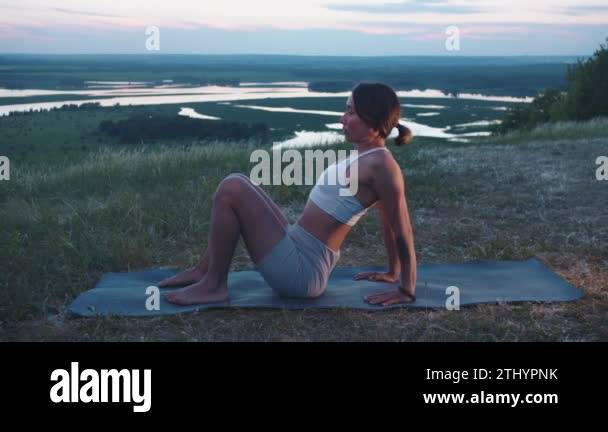 A slim woman practices on a hill on a yoga mat. Mid shot Stock