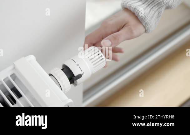 The woman turns the regulator of the thermostatic valve of the radiator ...