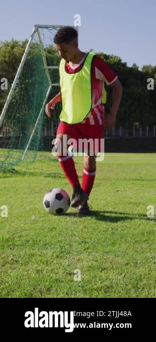 Vertical video of biracial football player on field kicking ball. Male ...