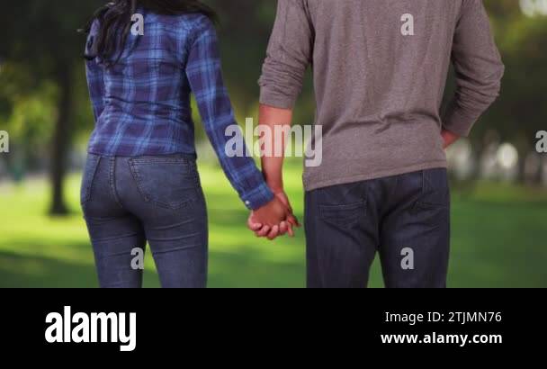 Rear view of young black couple holding hands in public park looking at ...