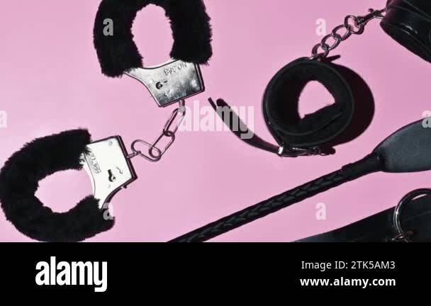 Handcuffs, whip flogger for BDSM sex with submission and domination. A set  of adult intimate erotic sex toys on a pink background
