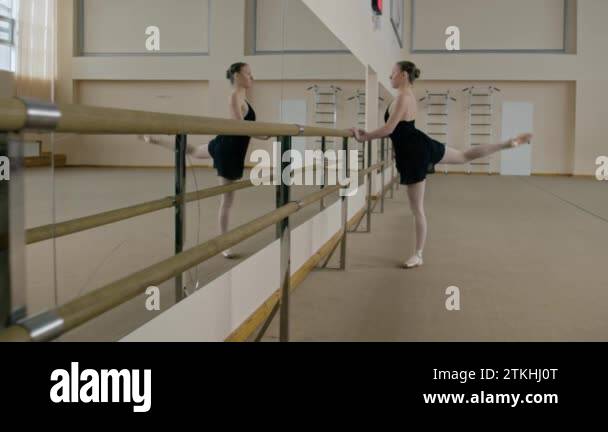 Ballerina in training bodysuit stands in front of ballet barre at dance ...
