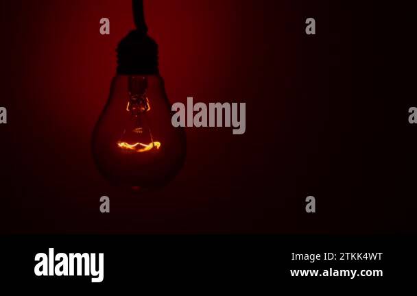 Light bulb lights up and goes out on a red background in the dark. Slow ...