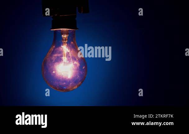 Light bulb goes out on a blue background in the dark. Slow turning off ...