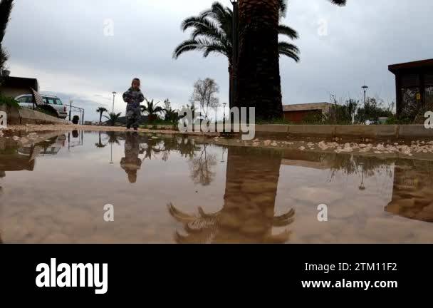 Little girl in rubber boots and overalls walks through a puddle on a ...