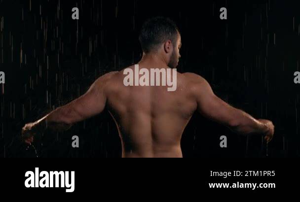 Nude male bodybuilder with big muscles standing back in the shower in