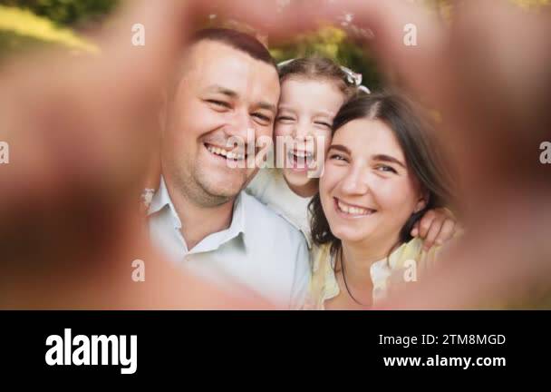 Dad, mom and daughter make a heart-shaped hand gesture. Family looking ...