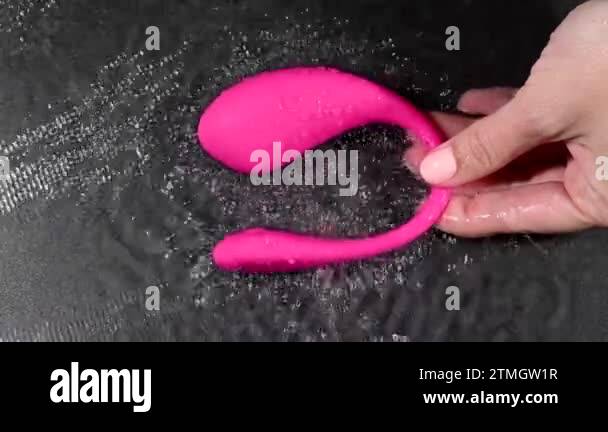 A woman is holding a pink vibrator in water. Sex toy on a black background